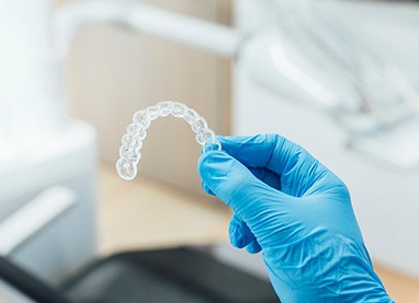 Dentist with blue glove holding clear aligner