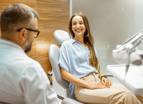 A woman sitting in a dental chair speaking with a dentist